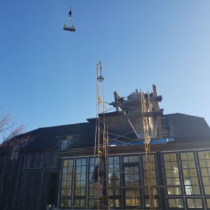 Crane lifting materials at a construction site with scaffolding and a wooden building under renovation, showcasing Kraneworks' crane services in action.