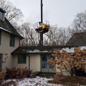 Crane lifting equipment above residential roof during winter, showcasing Kraneworks crane services in action for home installations.