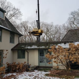 Crane lifting equipment above residential roof during winter, showcasing Kraneworks' professional crane services in action.