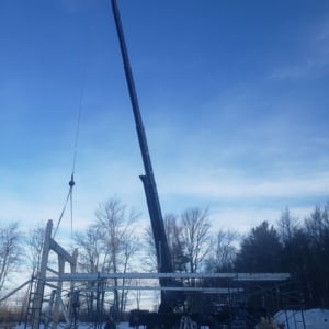 Crane lifting construction materials against a clear blue sky, showcasing Kraneworks' crane services in action at a project site.
