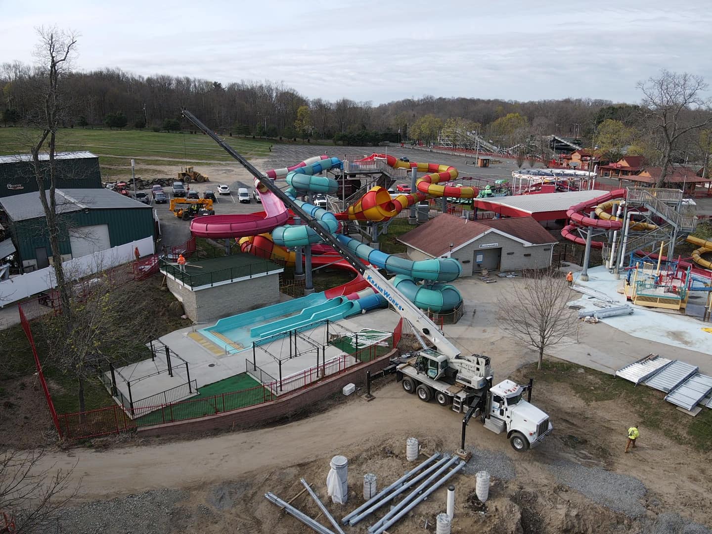 Boom truck lifting equipment at a water park construction site with colorful water slides and workers visible, showcasing the crane's versatility for residential and commercial projects.